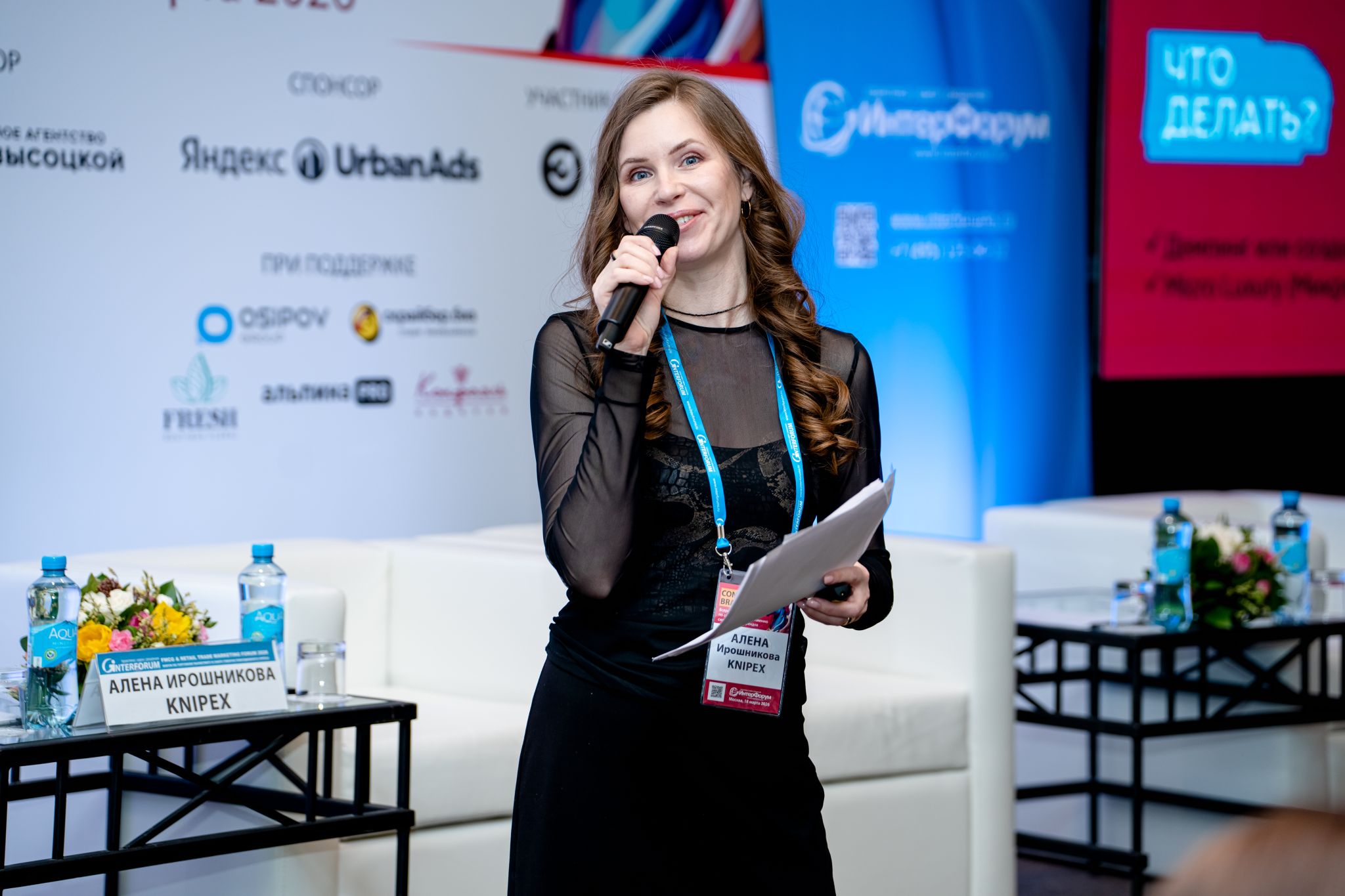 Алена Ирошникова выступает на деловом форуме с микрофоном